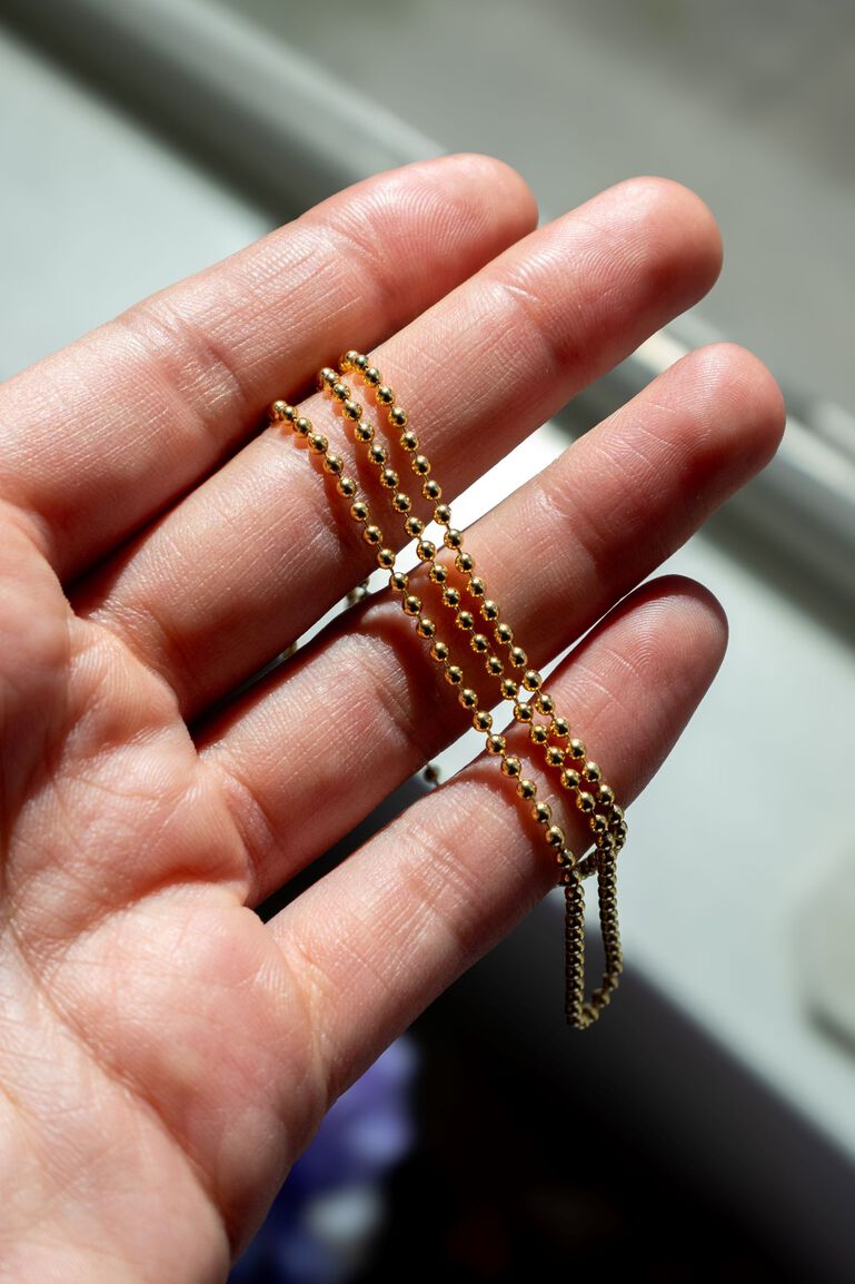 A yellow gold beaded necklace draped over a woman's fingers