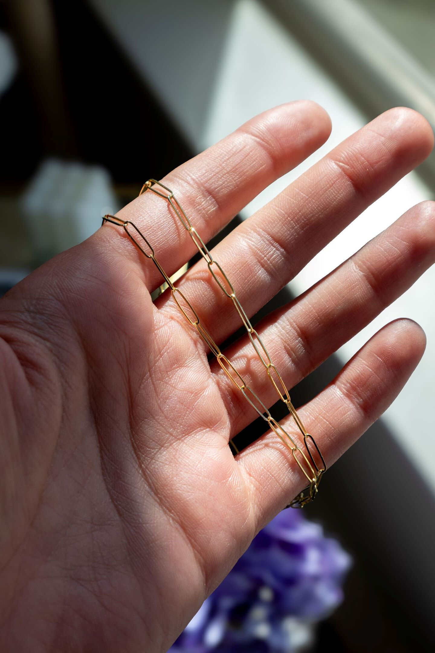A yellow gold paperclip chain is draped across a woman's fingers