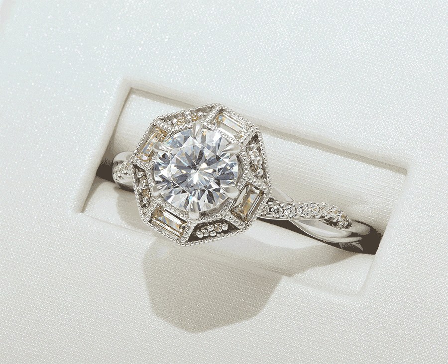 An engagement ring set in white gold features a sparkling round diamond centerpiece bordered by baguette and round diamonds - with even more round diamonds accenting the twisted shank.